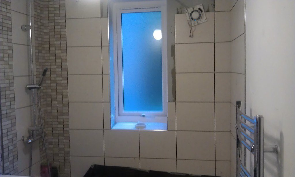 Clean tiled shower with a frosted window and a chrome rail